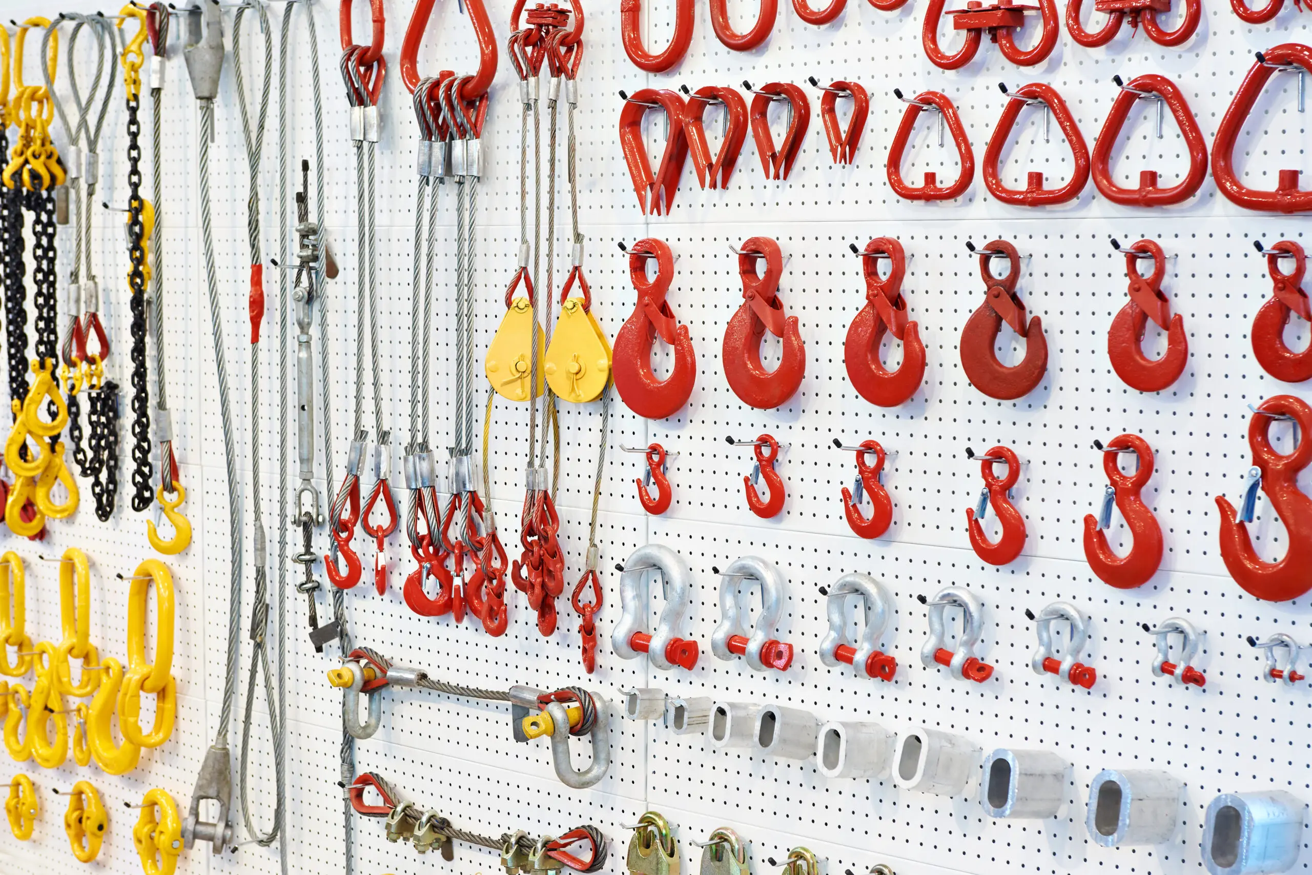 Lifting equipment, hooks and chains Various red hooks and lifting equipment displayed on a white pegboard.