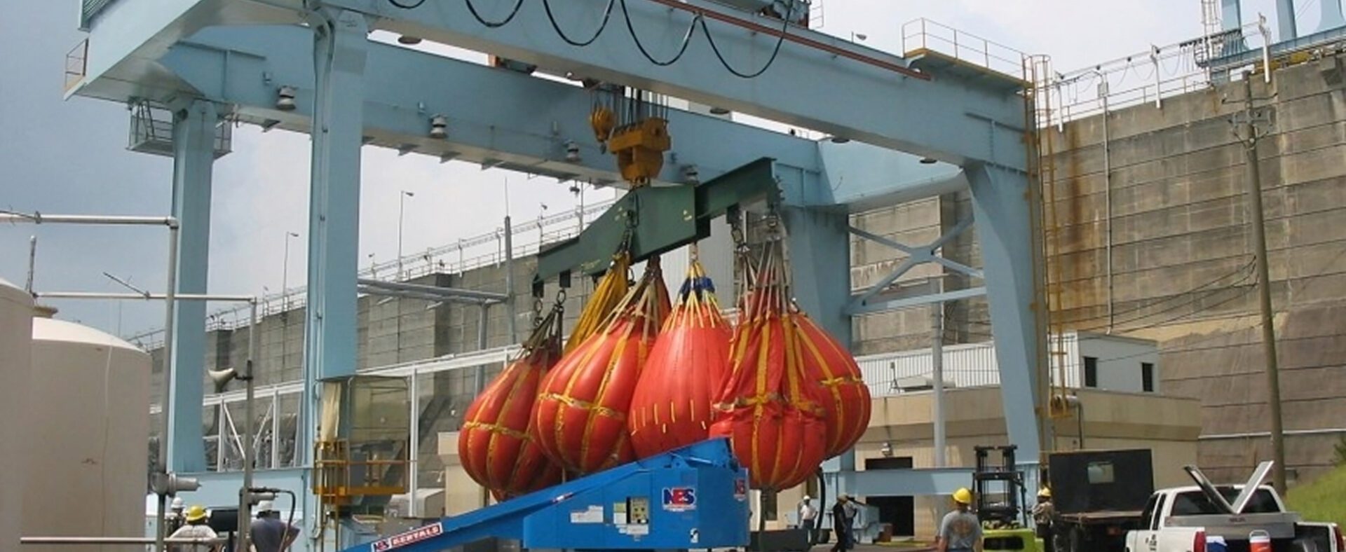 Crane lifting multiple large red load bags.